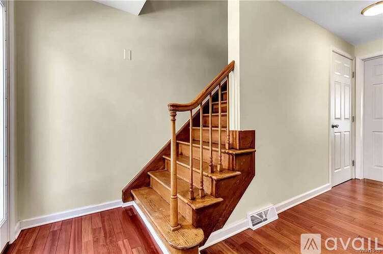 A wooden staircase with a white wall and a door in the background.