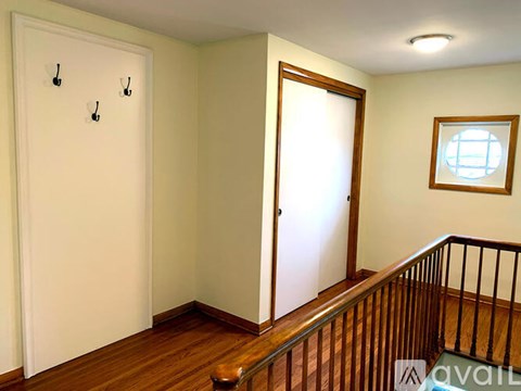 A room with a wooden floor, a white door, a window, and a staircase.