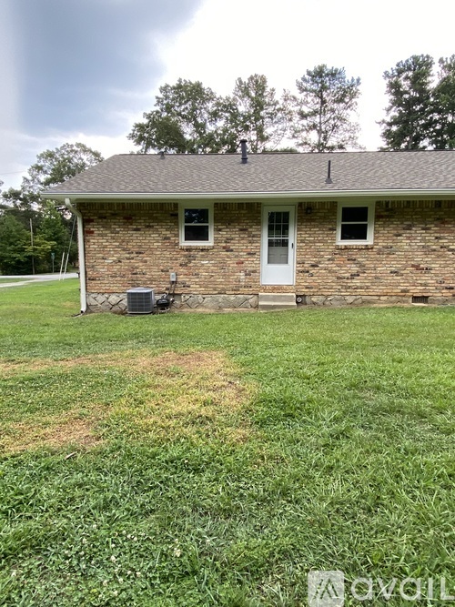 A small house with a white door and windows is surrounded by a grassy area.