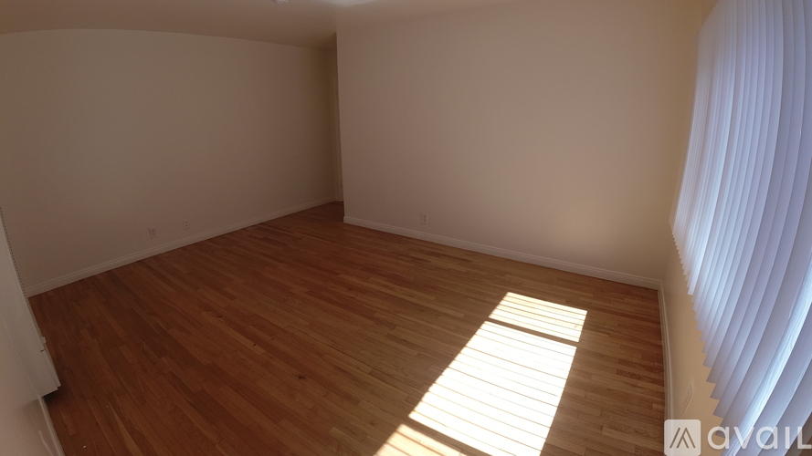 A room with wooden flooring and a window with white curtains.