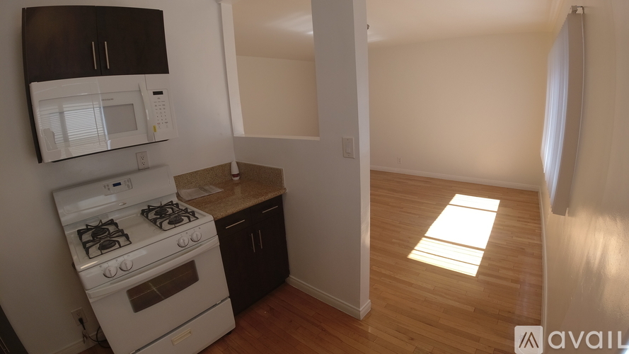 A kitchen with a white stove and microwave, wooden floors, and a window letting in sunlight.
