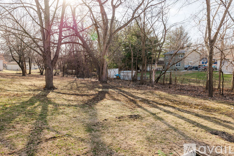 A field with trees and a house in the background.