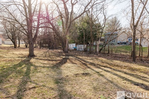 A field with trees and a house in the background.