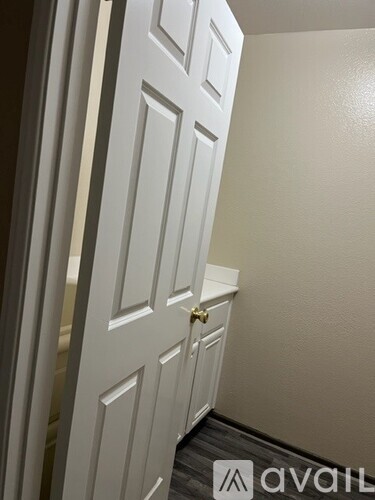 A white door with a gold handle is in a room with a wooden floor.