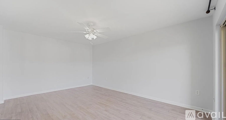 A spacious room with a ceiling fan and light fixture, and a wooden floor.