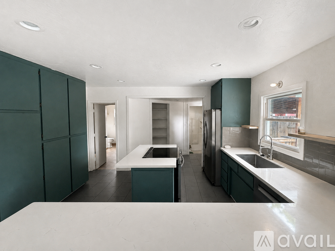 A modern kitchen with dark green cabinets and a white countertop.