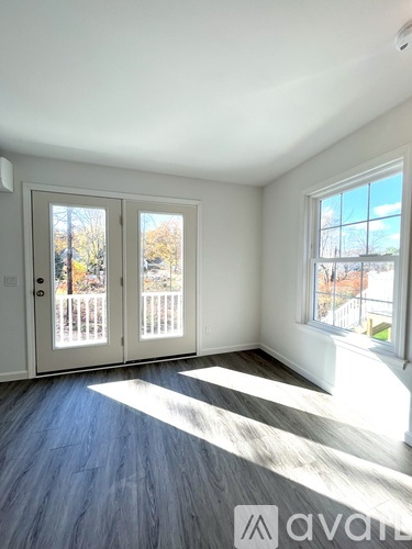 A room with a white door and a window with a view of a fence and trees.