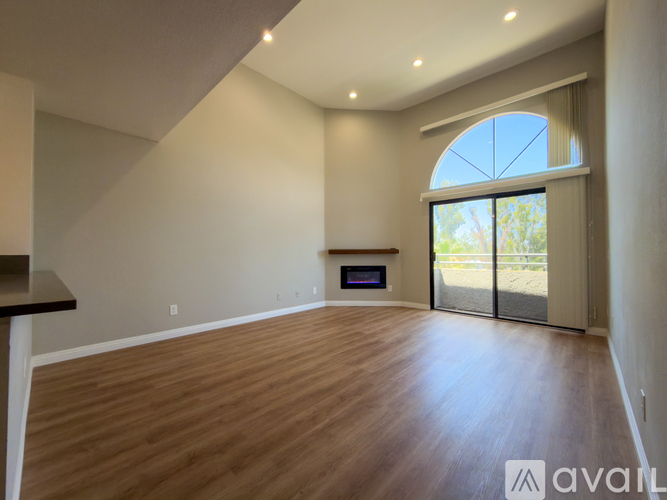 A spacious room with wooden flooring and a large window with a view of trees.