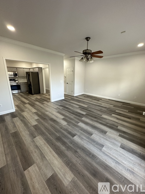 A room with a ceiling fan and a kitchen in the background.