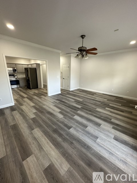 A room with a ceiling fan and a kitchen in the background.