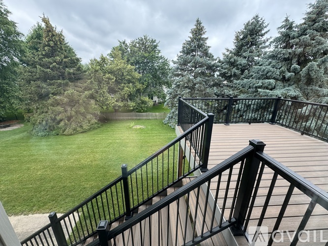 A deck with a black railing overlooks a green lawn and trees.