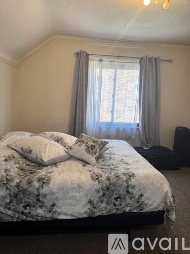 A bedroom with a bed, a window with curtains, and a chair.