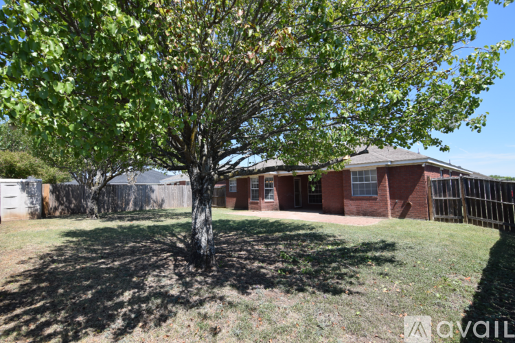 A tree with green leaves is in the foreground of a grassy area with a house in the background.
