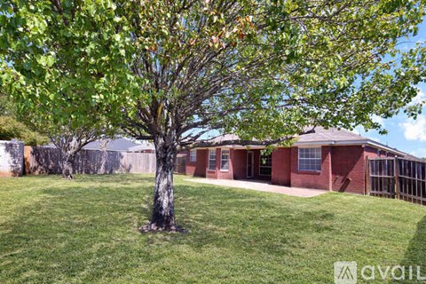 A tree with green leaves is in the foreground of a grassy area with a house in the background.