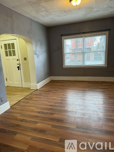 A room with wooden flooring and a window overlooking a red building.