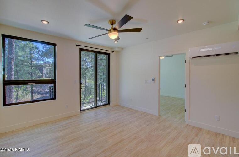 A spacious room with a ceiling fan and sliding glass doors leading to a wooded area.