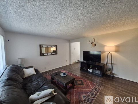 A living room with a black leather couch and a flat screen TV mounted on the wall.