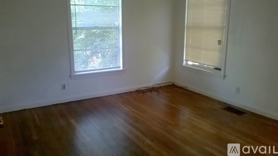 A room with wooden floors and two windows, one with blinds.