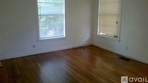 A room with wooden floors and two windows, one with blinds.