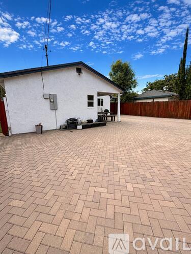 A house with a white exterior and a red door is surrounded by a brick patio.