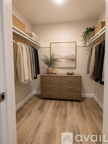 A well-lit, spacious walk-in closet with a wooden floor and a framed picture on the wall.