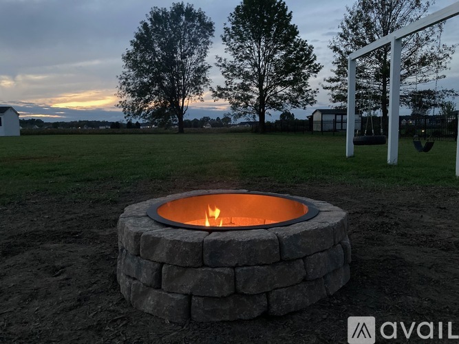 A stone fire pit with a fire burning inside is in the foreground of a grassy field.