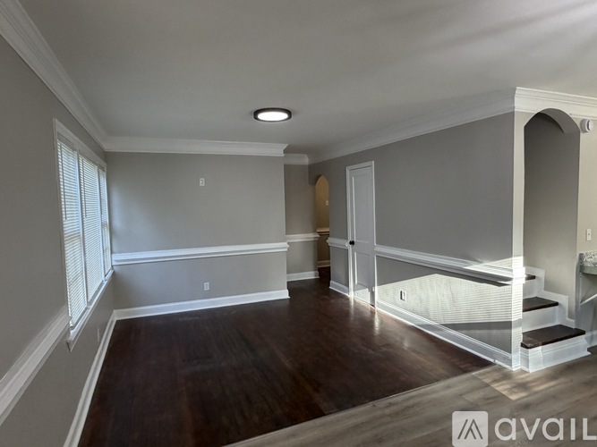 A spacious room with wood flooring and a staircase leading to the upper level.