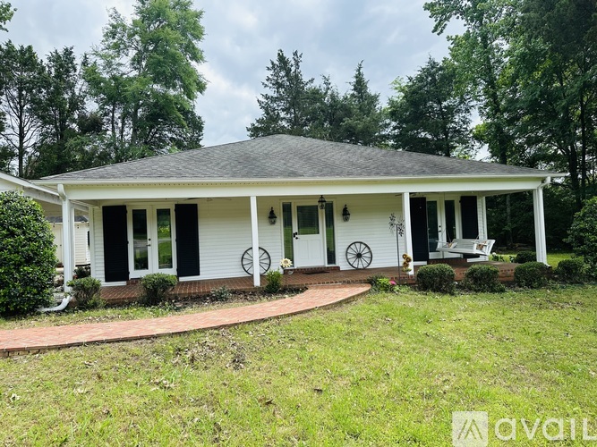 A white house with a black roof and a porch with a brick walkway.