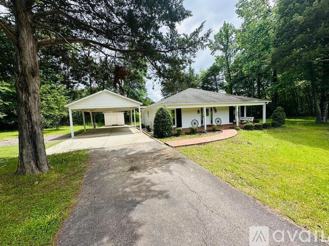 A white house with a porch is surrounded by greenery.