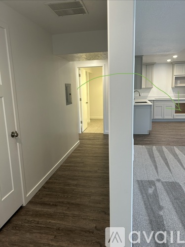 A hallway with a door on the left and a kitchen in the background.