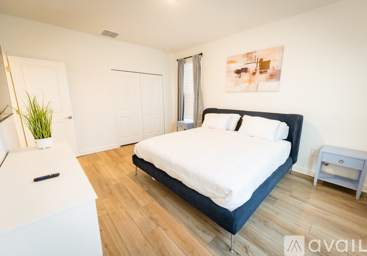 A bedroom with a large bed, a small table, and a plant on the nightstand.
