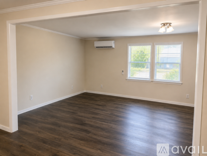 A spacious room with wooden flooring and a window with blinds.