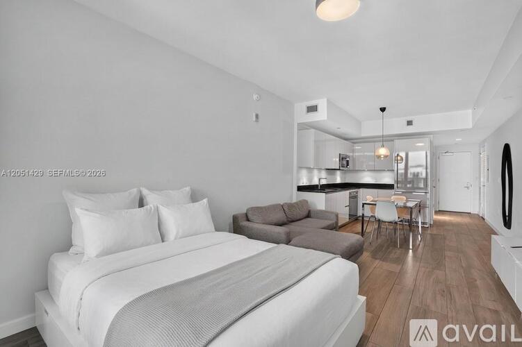 A bedroom with a large bed and a kitchen area in the background.