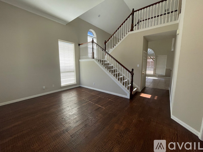 A spacious room with wooden floors and a staircase leading to another level.