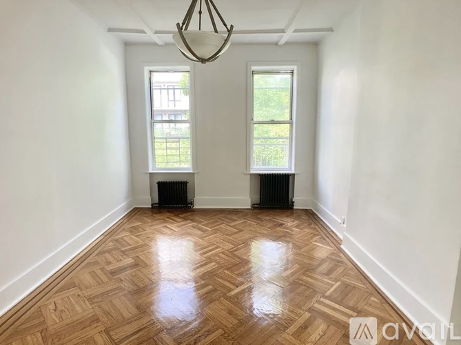 A room with wooden flooring and two windows.