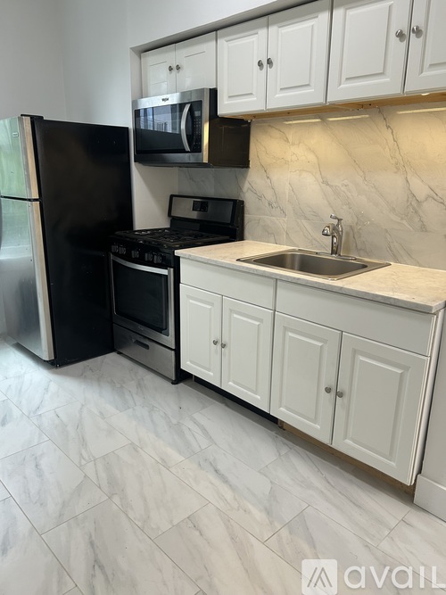 A kitchen with a black fridge, white cabinets, and a marble backsplash.