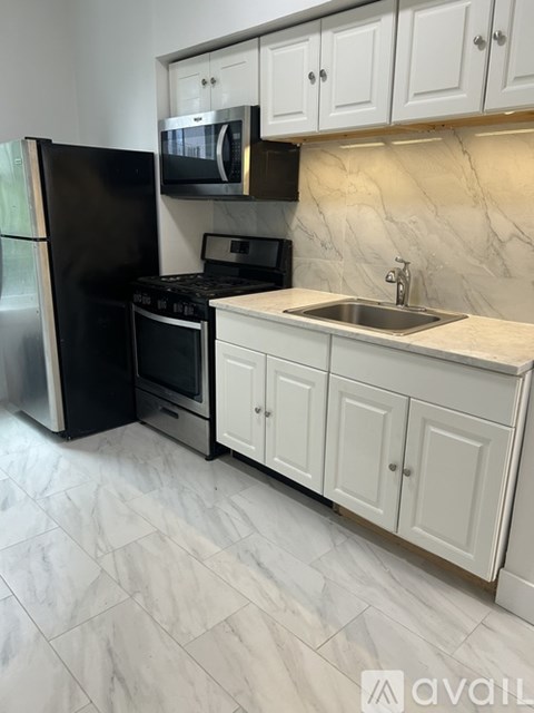 A kitchen with a black fridge, white cabinets, and a marble backsplash.