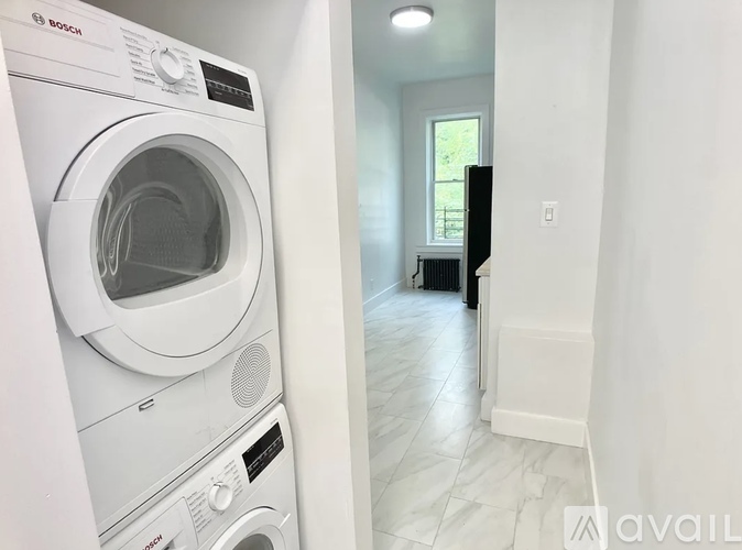 A Bosch washing machine is in a room with a tiled floor and a window.