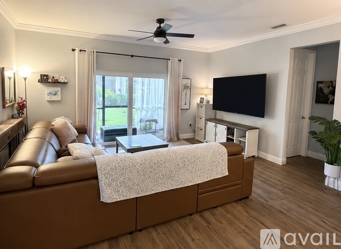 A living room with a white chair, a wooden coffee table, and a large window with a view of greenery outside.
