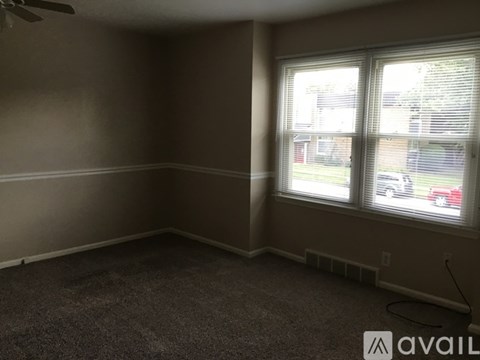 A room with a carpeted floor, a ceiling fan, and a window with blinds.