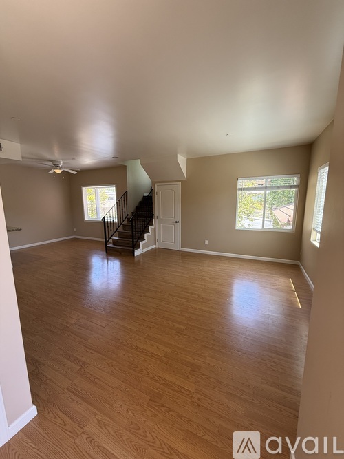 A spacious room with wooden flooring and a staircase.
