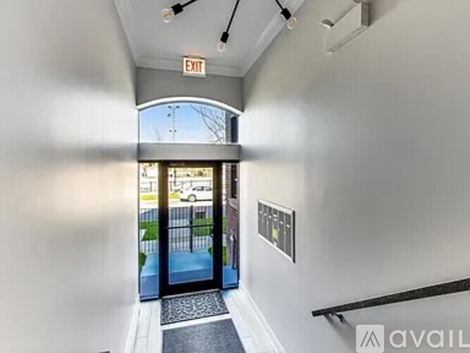 A hallway with a black mat on the floor leading to a glass door with an exit sign above it.
