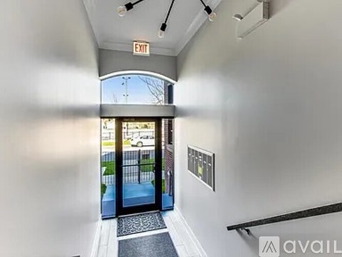 A hallway with a black mat on the floor leading to a glass door with an exit sign above it.