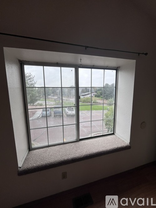 A window with a view of a parking lot and trees.
