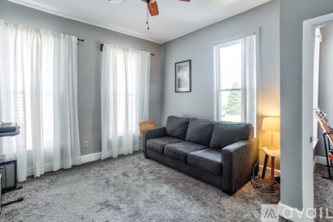 A living room with a grey couch and a window with white curtains.