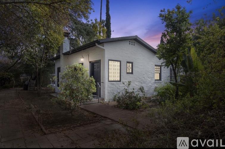 A house with a dark front door is surrounded by trees and bushes.