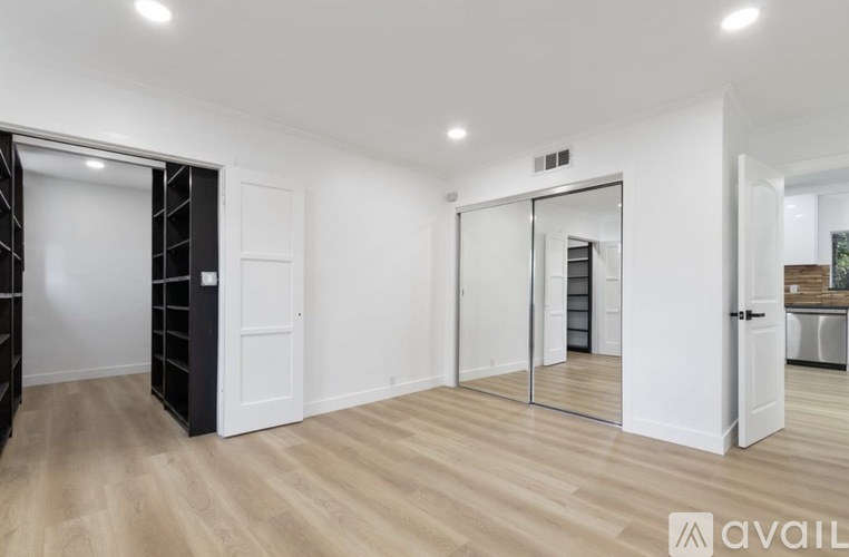 A room with white walls and wooden flooring, featuring a black shelving unit and a glass door leading to another room.