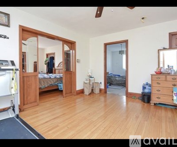 A room with wooden floors and a mirrored doorway leading to a bedroom.