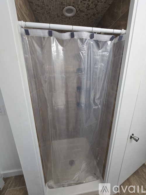 A shower with a plastic curtain and a drain.