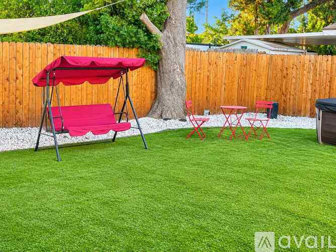 A red canopy is over a red chair and table in a backyard.